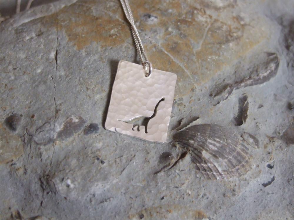 Silver Dinosaur pendant: A textured sterling silver pendant showing a silhouette of long necked Dinosaur.