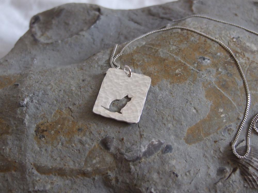 Silver cat pendant: A cat sits peacefully taking in the world around her on a background of textured sterling silver.